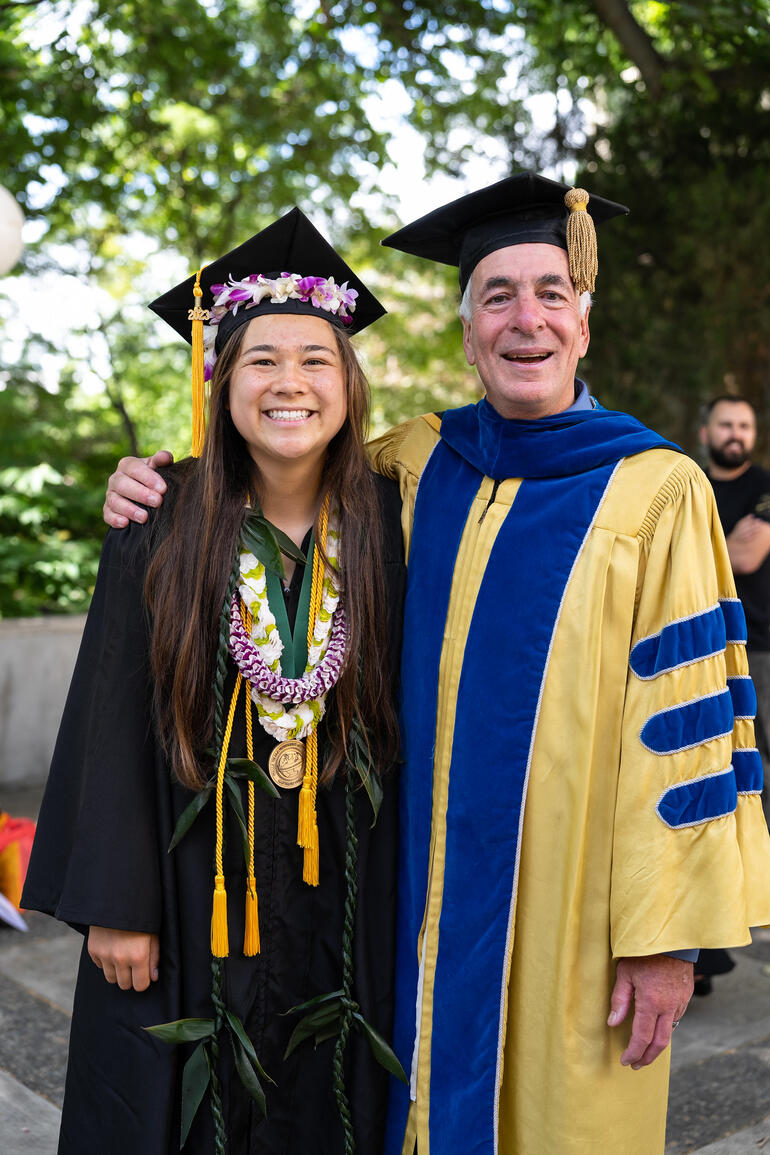 Female graduate smiles next to male professor in regalia at Walla Walla University.