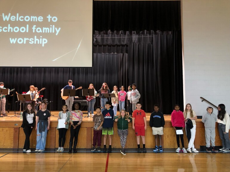 students stand on stage and in front of stage for chapel