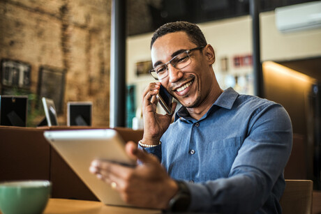 A man talks on phone while holding a tablet.