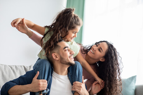 Smiling parents with little girl on father's shoulders.