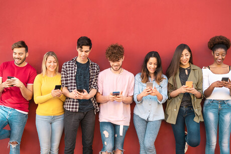 A group of young adults standing and looking at their phones.