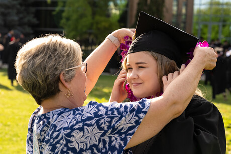 Woman helps female student adjust graduation cap.
