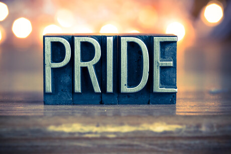 The word PRIDE written in vintage metal letterpress type on a soft backlit background.