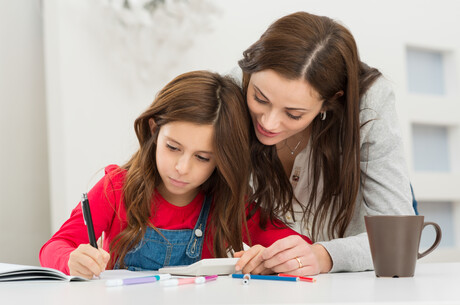 Happy Young Mother Helping Her Daughter While Studying At Home