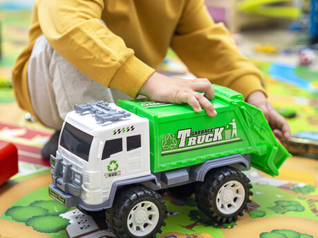 Child boy playing with a garbage truck toy on room floor at home - kid hands playing educational vehicle for learning sustainability and recycling. Toddler being creative and curious