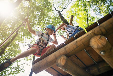 Kids working together on difficult ropes course in adventure park. Sunny summer day.