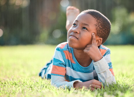 Child on grass looking up and thinking