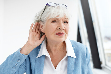 Come again please? Stylish retired female in elegant clothes holding hand at her ear