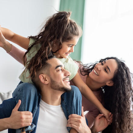 Smiling parents with little girl on father's shoulders.
