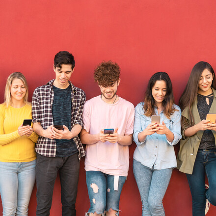 A group of young adults standing and looking at their phones.