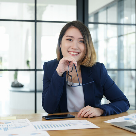 A business woman sits at desk and smiles.