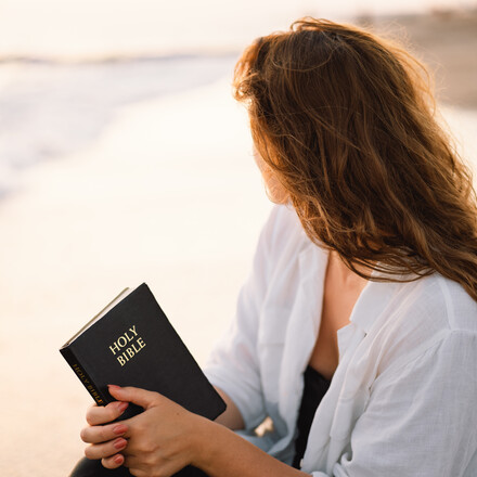 Christian woman holds bible in her hands. Reading the Holy Bible on the sea during beautiful sunset. Concept for faith, spirituality and religion. Peace, hope