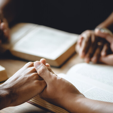 Hands clasped on top of open Bibles on a table