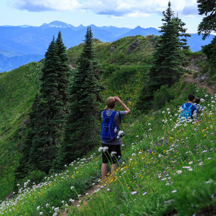 Student uses binoculars while hiking on mountain trail