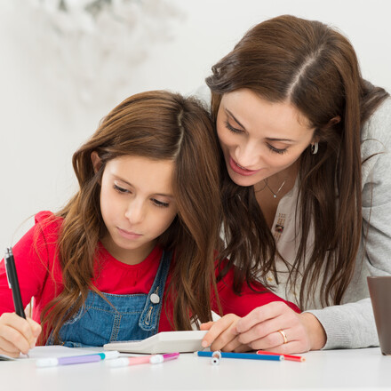 Happy Young Mother Helping Her Daughter While Studying At Home