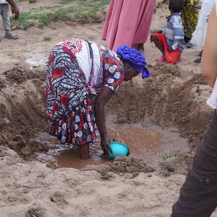 Woman scoops water from muddy puddle