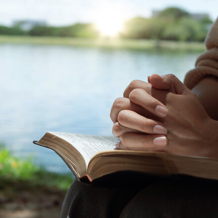 Woman hands praying with a bible in his legs Outdoors