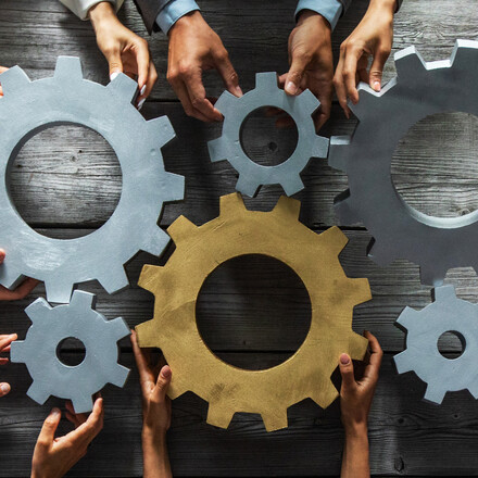 Group of business people joining together silver and golden colored gears on table at workplace top view