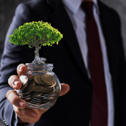 businessman holding jar of coin with small tree growing up