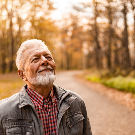 Tranquil senior man enjoying a walk on forest road on autumn day and breathing fresh air with eyes closed.