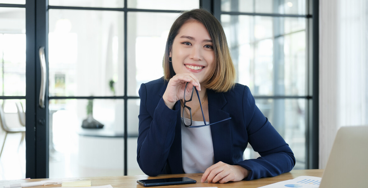 A business woman sits at desk and smiles.