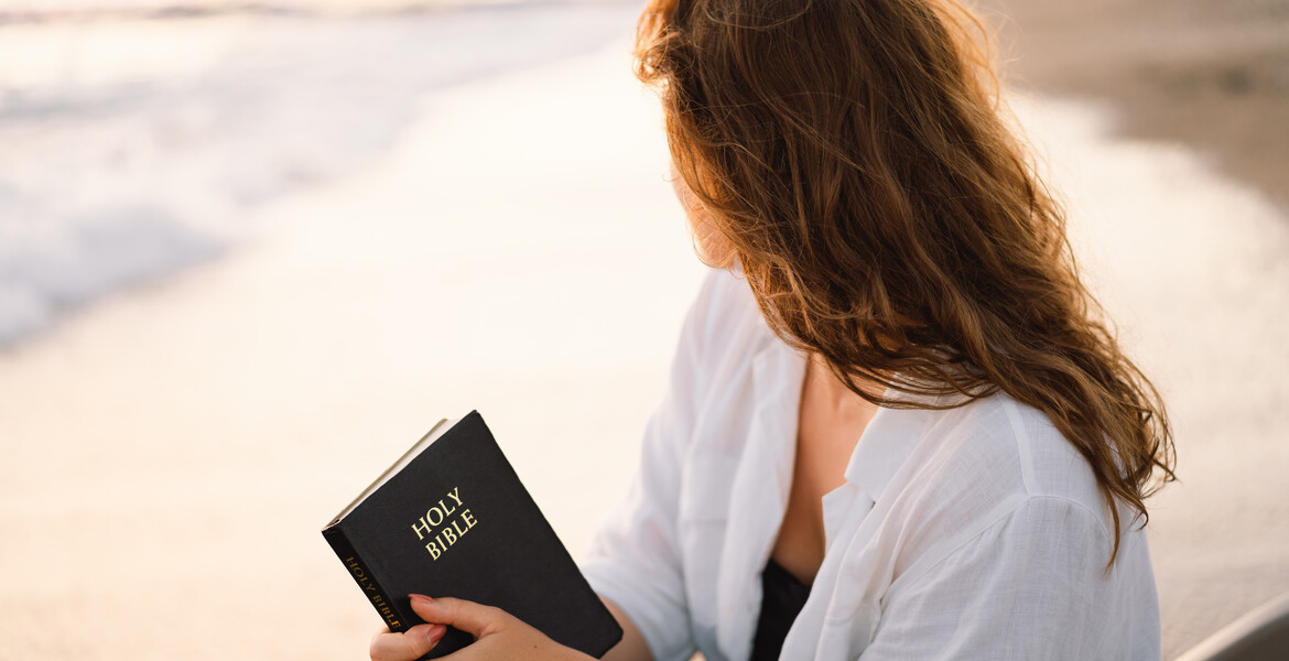 Christian woman holds bible in her hands. Reading the Holy Bible on the sea during beautiful sunset. Concept for faith, spirituality and religion. Peace, hope