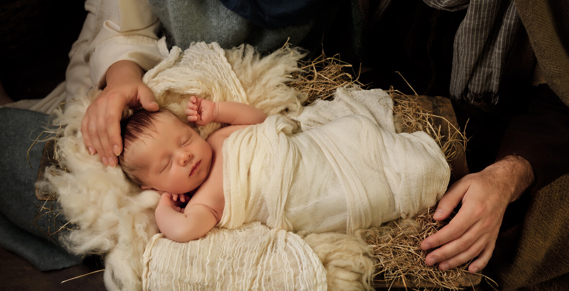 Parents' hands caring for their 9 days old baby boy in an authentic Christmas nativity scene