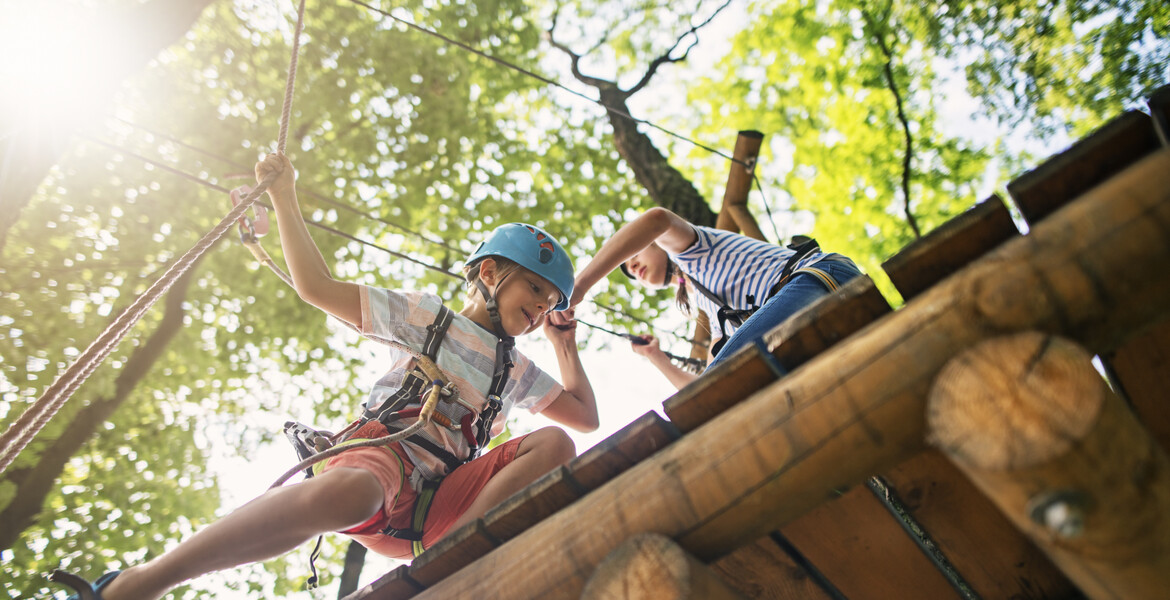 Kids working together on difficult ropes course in adventure park. Sunny summer day.